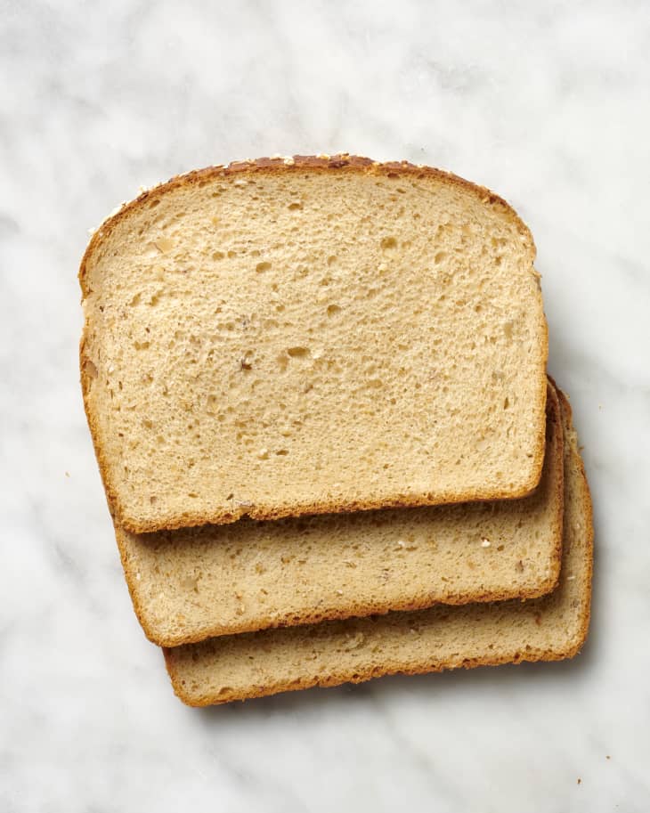 Overhead view of three slices of whole grain bread on a marble surface.