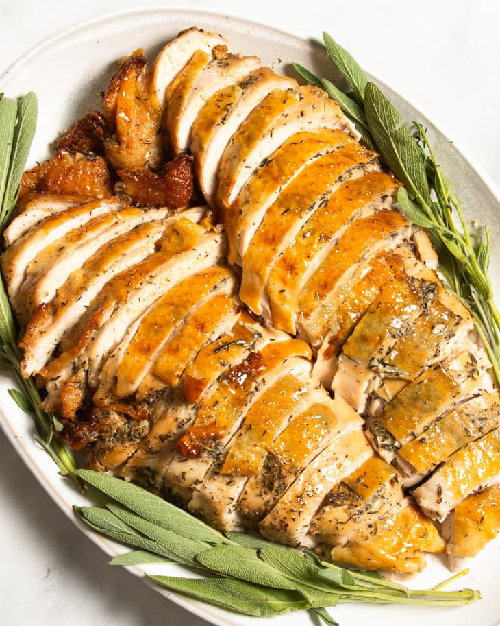 Overhead view of sliced roast turkey on a white platter with sage.