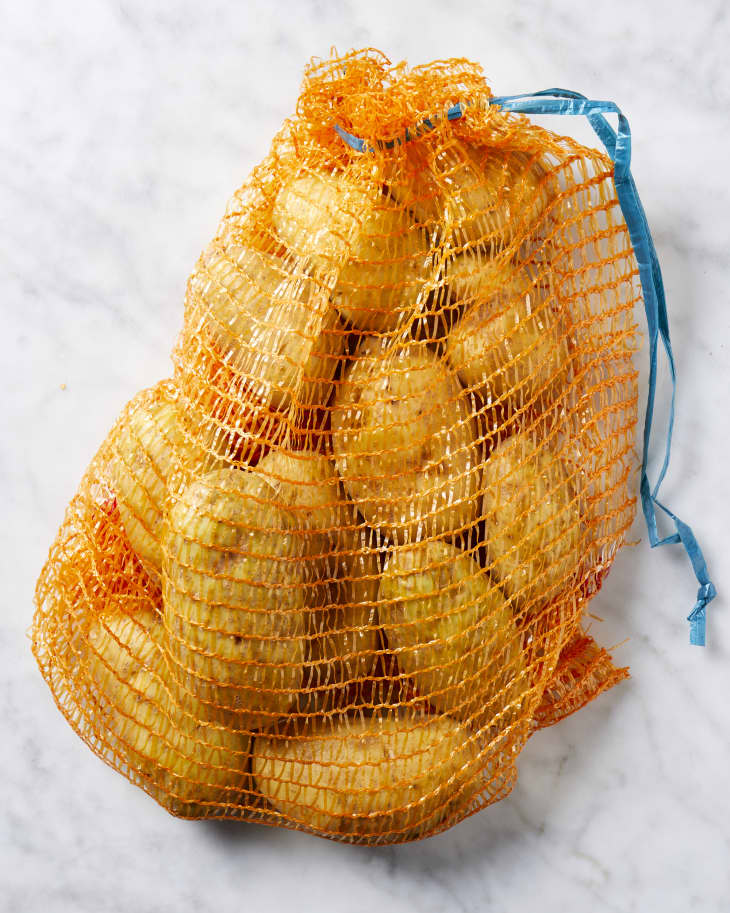 Overhead view of a plastic mesh bag full of potatoes on a marble counter.