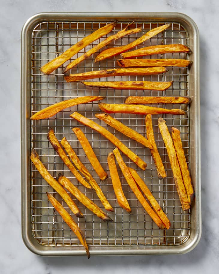 Overhead view of baked sweet potato fries on a cooling rack in a baking sheet.