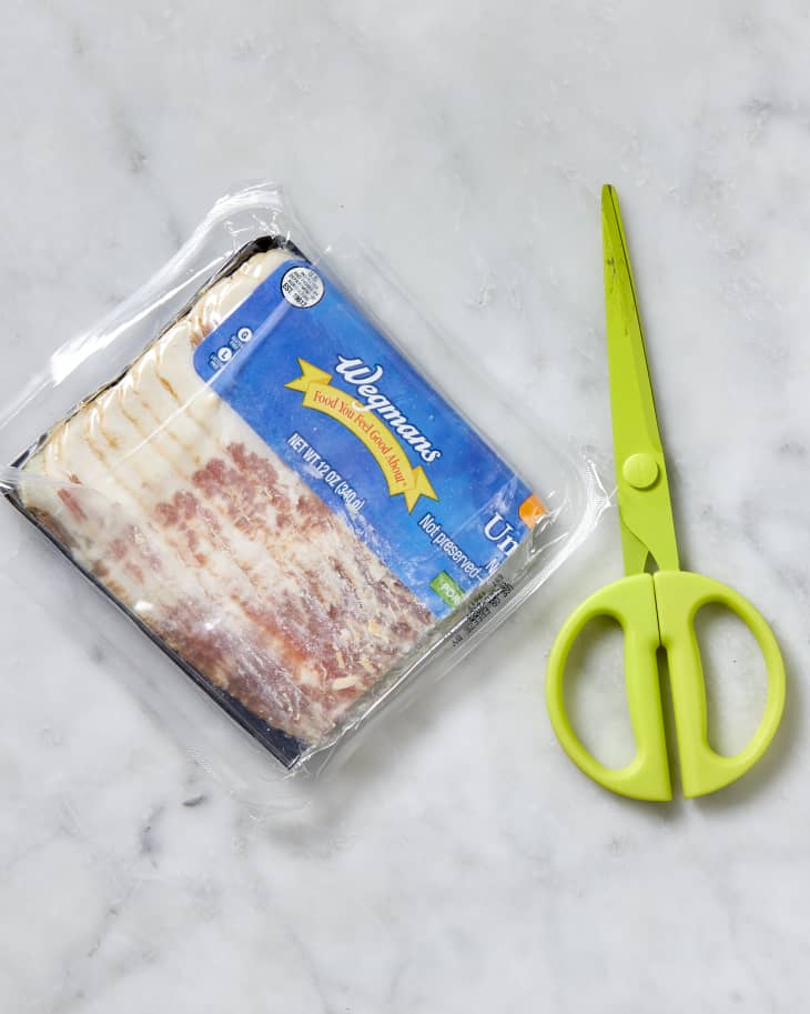 Overhead shot of bacon being wrapped in the empty plastic it came in and a pair of green scissors next to it.