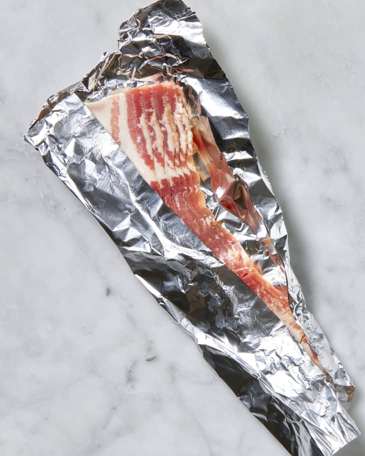 Overhead shot of bacon being wrapped in tin foil.