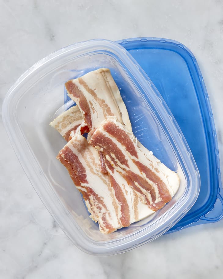 Overhead shot of bacon being saved in a plastic Tupperware container.