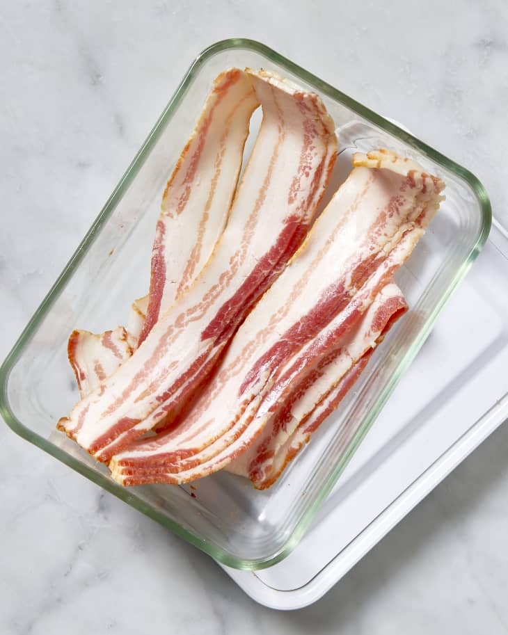 Overhead shot of bacon being stored in a glass Tupperware container.