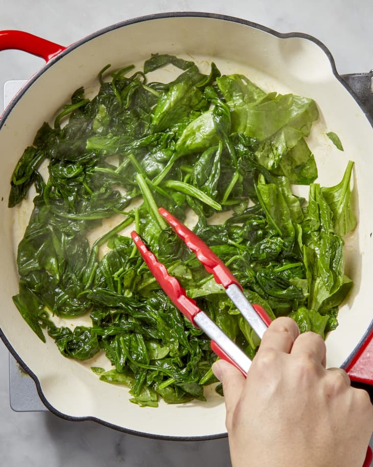 Overhead shot of spinach being cooked down in a pan, and stirred by a tongs