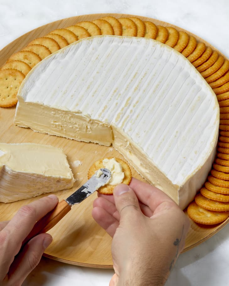 Angled shot of hand spreading brie onto a ritz cracker.