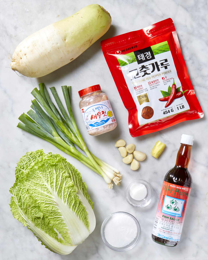 Overhead shots of the ingredients needed to make kimchi, on a white marble surface.