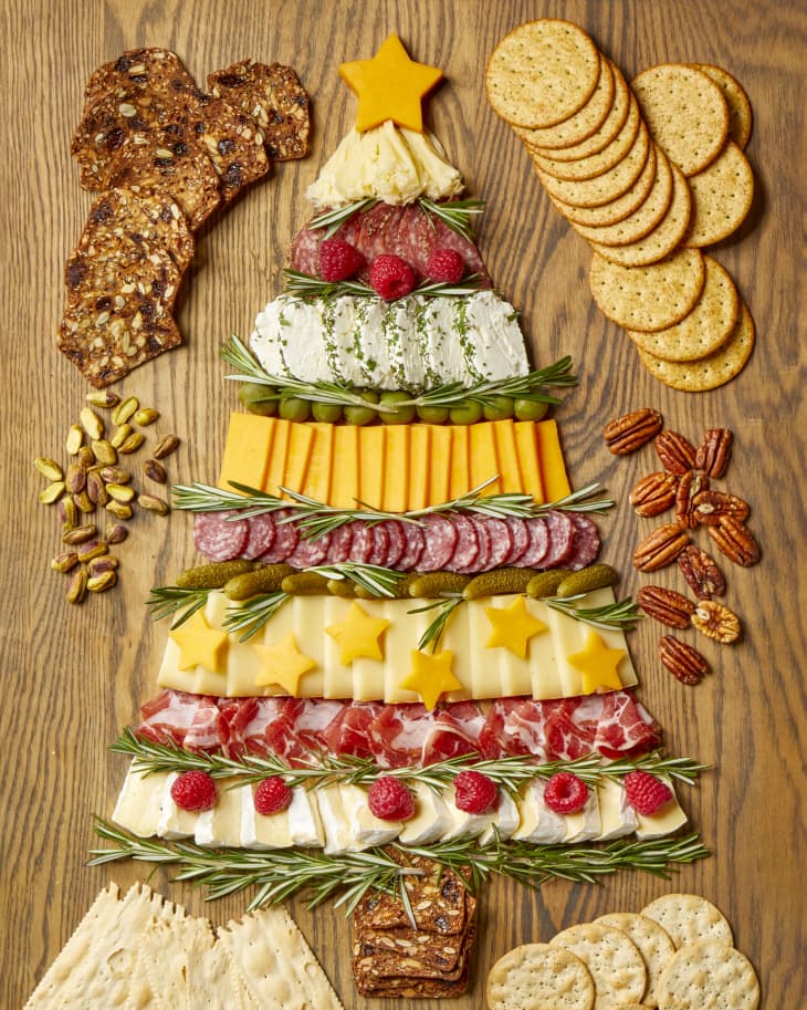 Overhead shot of a charcuterie board in the shape of a christmas tree, with assorted crackers scattered along the edge of the board.