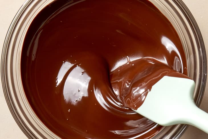 Overhead shot of melted chocolate in a glass bowl with a blue spatula stirring it.