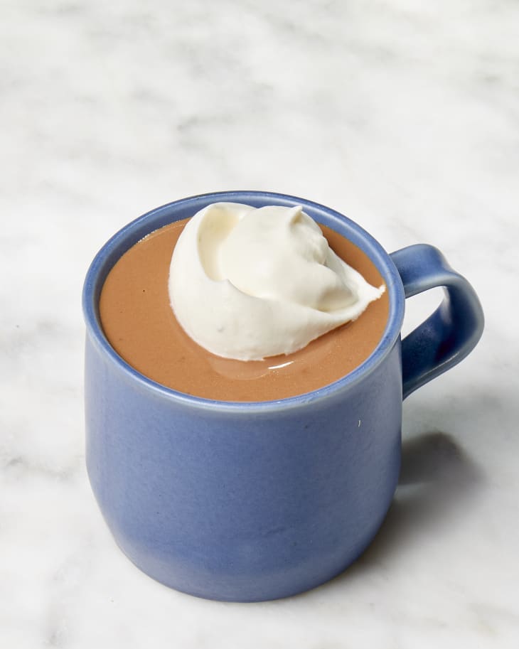 Angled shot of Jacques Torres' hot chocolate recipe in a dark blue mug, topped with whipped cream.