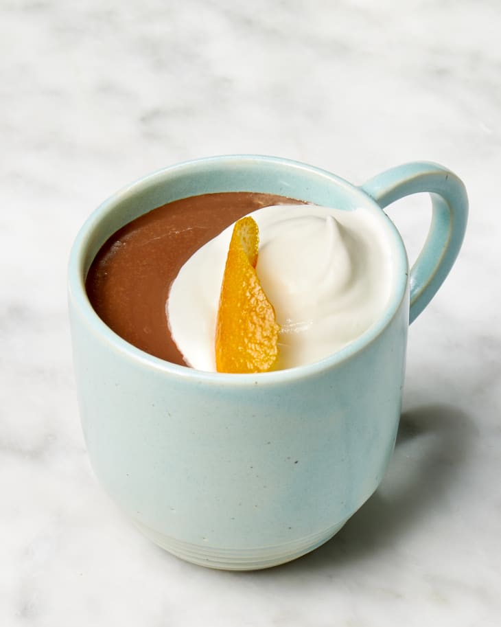 Angled shot of Carla Hall's hot chocolate recipe in a blue mug, topped with whipped cream and an orange peel.