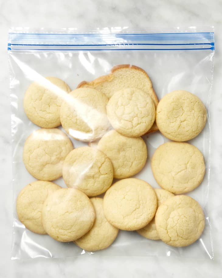 Overhead shot of sugar cookies in a gallon sized ziplock bag, with a single piece of white bread underneath the cookies.