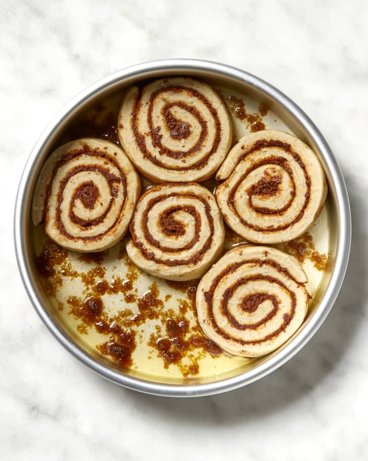 Overhead shot of five unbaked cinnamon rolls in a cake pan, with melted butter and brown sugar at the bottom.
