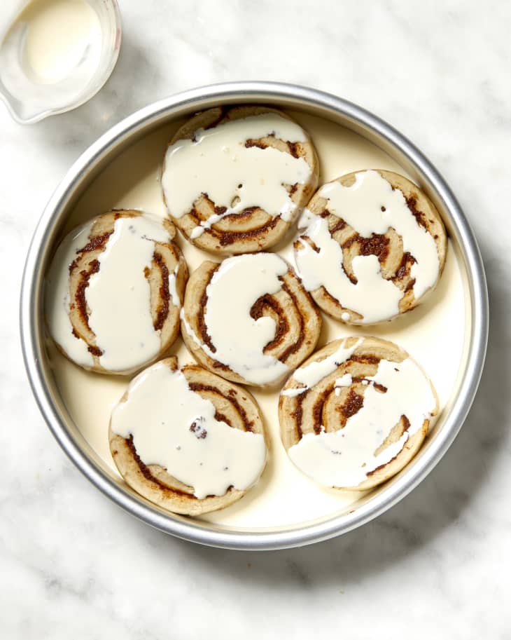 Overhead shot of unbaked cinnamon rolls in a cake pan covered in cream.