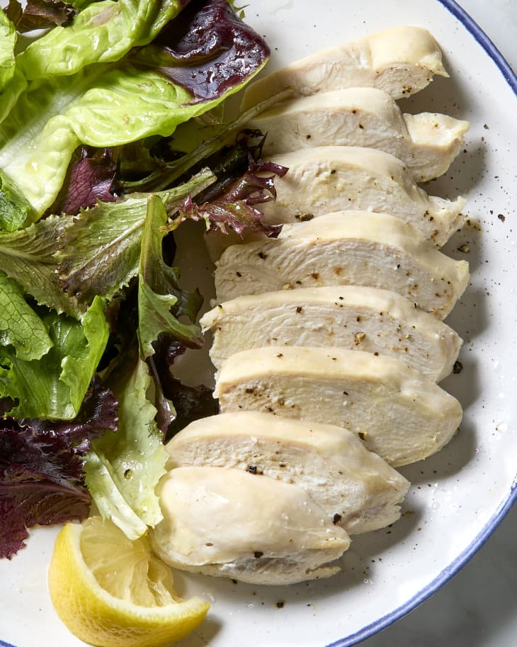 overhead shot of poached chicken on a plate with a side salad and lemon wedge.