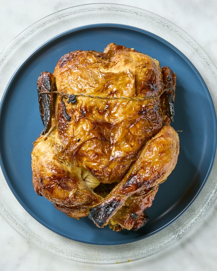 overhead shot of a rotisserie chicken on a dark blue plate in a microwave.