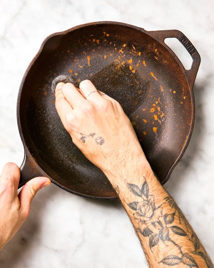 A hand scrubbing rust off of a cast iron skillet.
