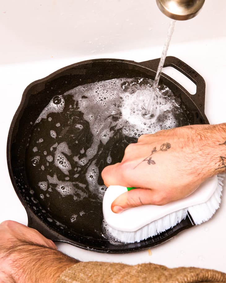 A hand scrubbing a cast iron skillet in a sink.