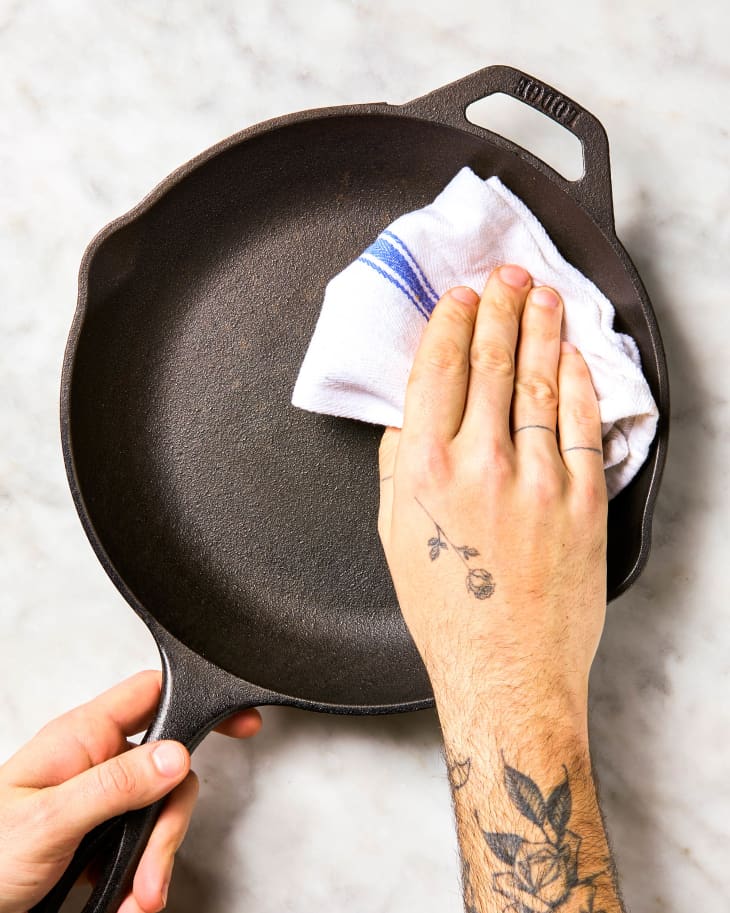 A hand wiping a cast iron skillet dry with a dish towel.