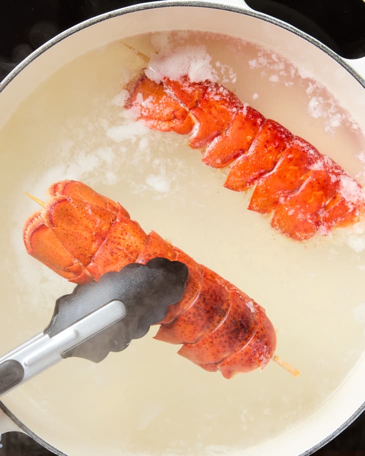 overhead shot of two lobster tails with a skewer through them in a pot of boiling water.
