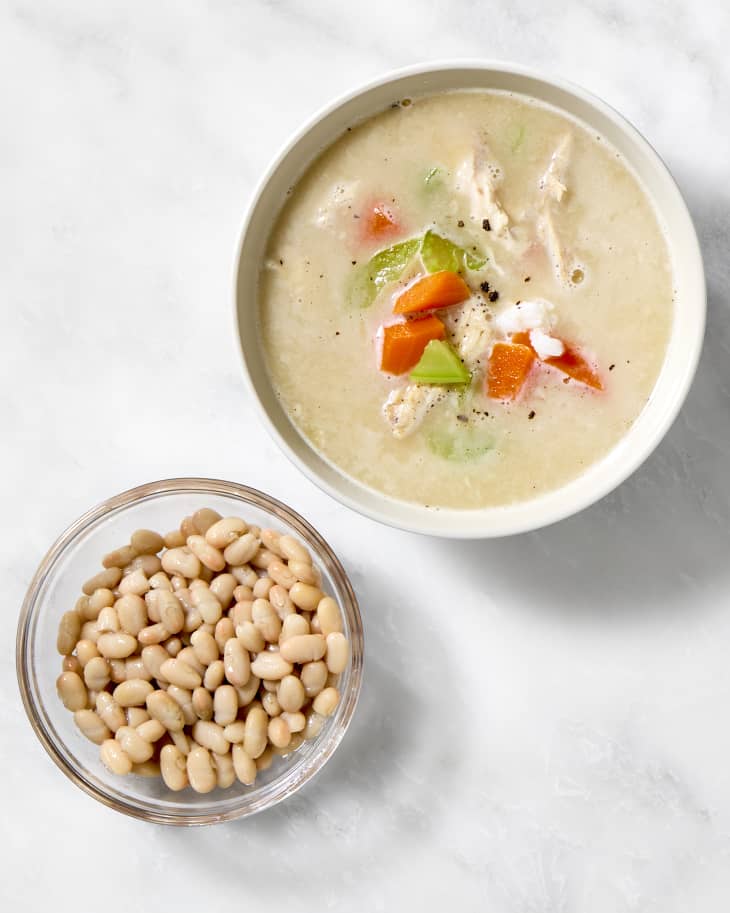 A bowl of chicken and rice soup with a bowl of white beans next to it.