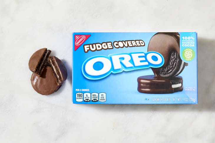 overhead shot of a box of fudge covered oreos, with a full and broken up fudge covered oreo to the left of the box