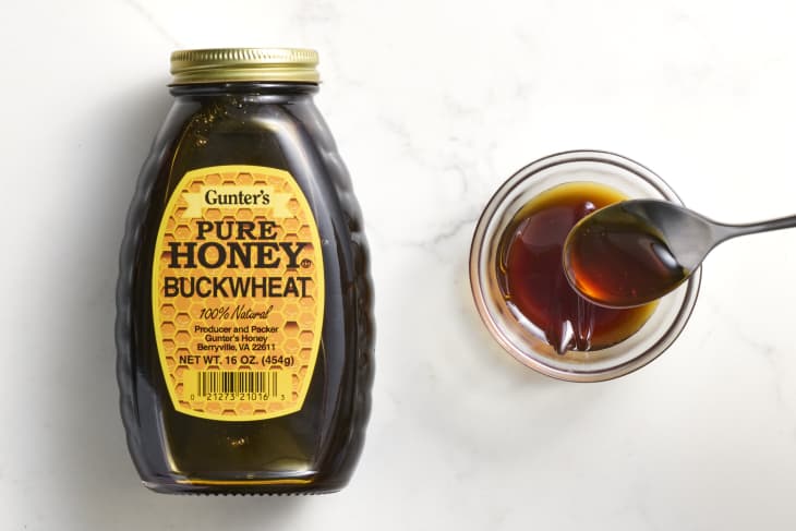 overhead shot of gunter's pure buckwheat honey in a bottle, with a small glass bowl of it to the right of the bottle.