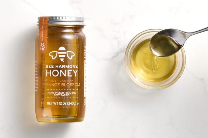 overhead shot of bee harmony's orange blossom honey on a white marble surface, with a small glass bowl of it to the right.