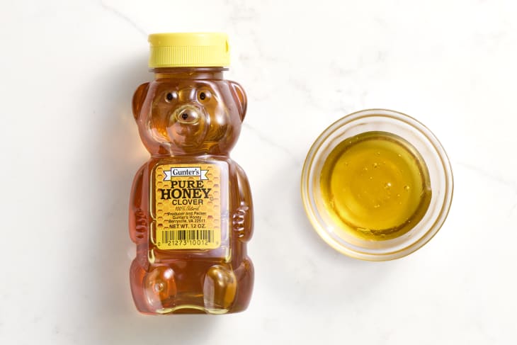 overhead shot of gunter's pure clover honey in a teddy bear bottle, with a small glass bowl of it to the right.