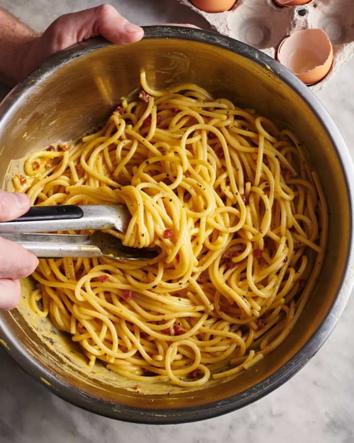 pasta carbonara being stirred in a mixing bowl