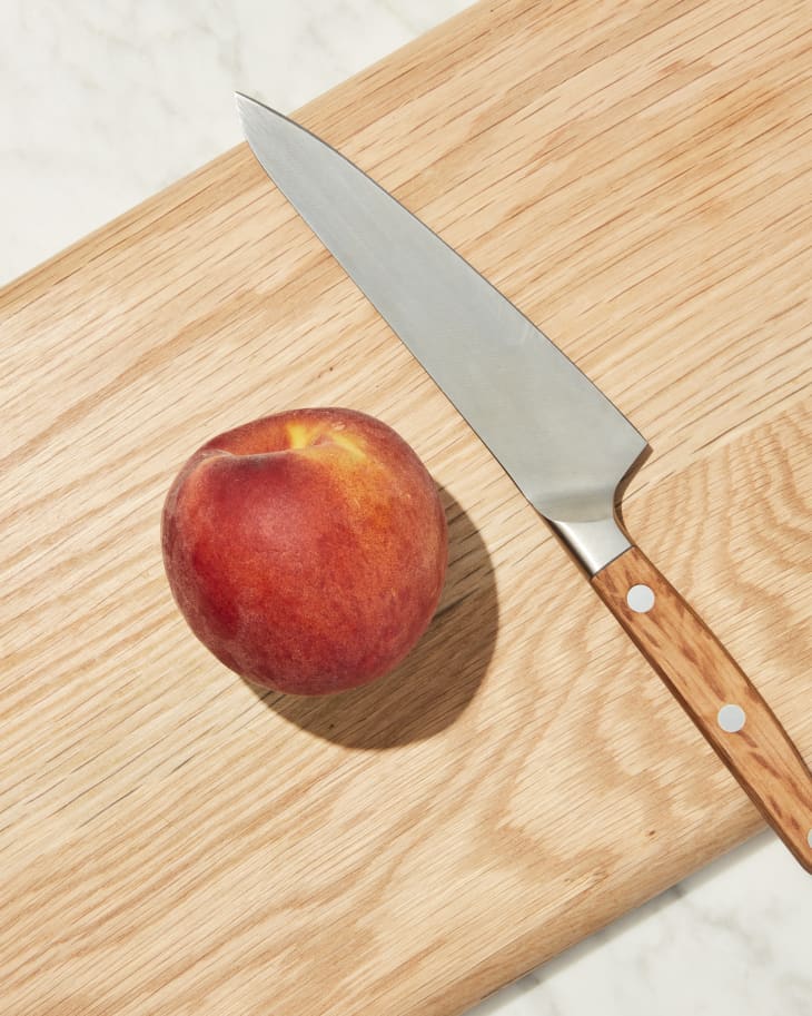 Peach on cutting board with knife laying beside.