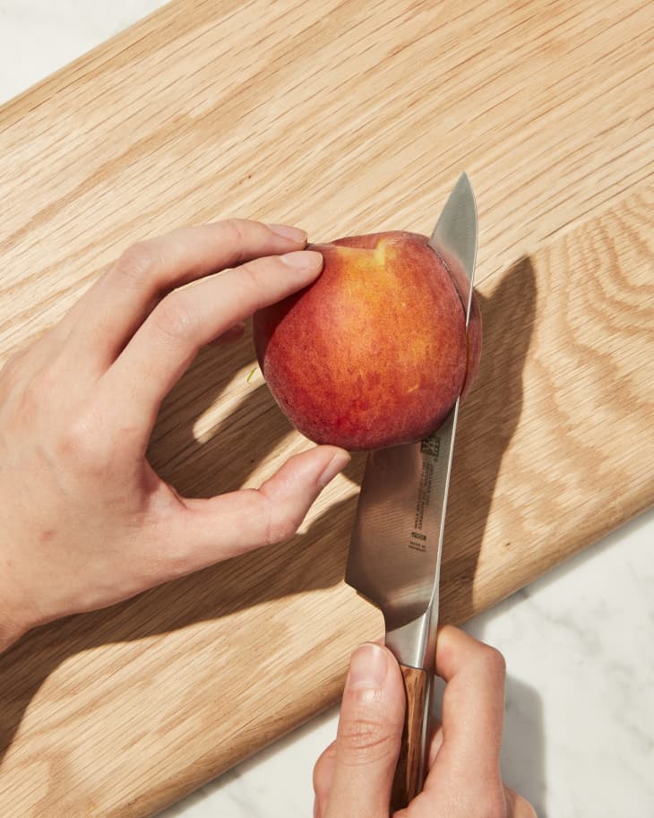 Someone slicing peach on cutting board.