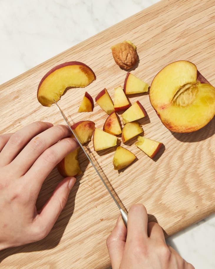 Cutting peach into cubes on cutting board.