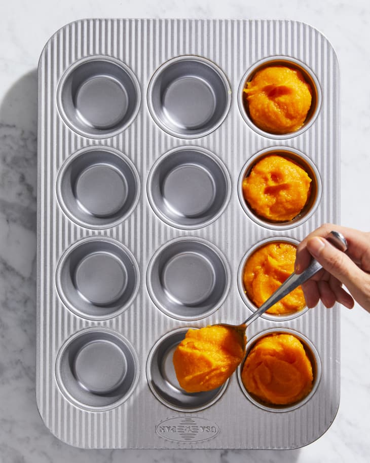 Someone spooning pureed butternut squash into muffin tin.