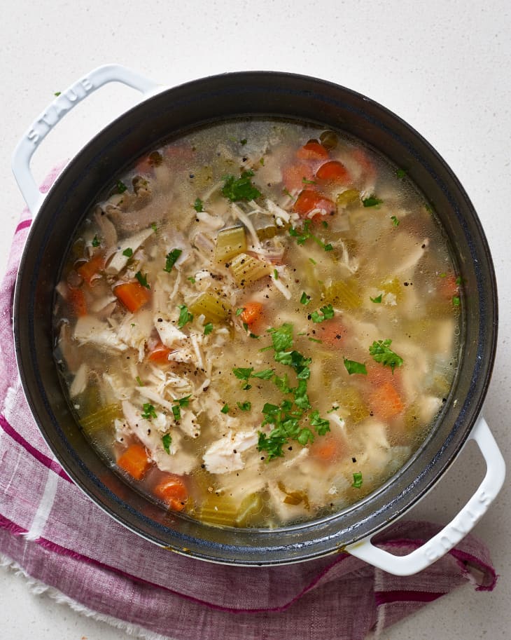 Chicken soup with carrots, celery, and rice, garnished with parsley, in a Dutch oven