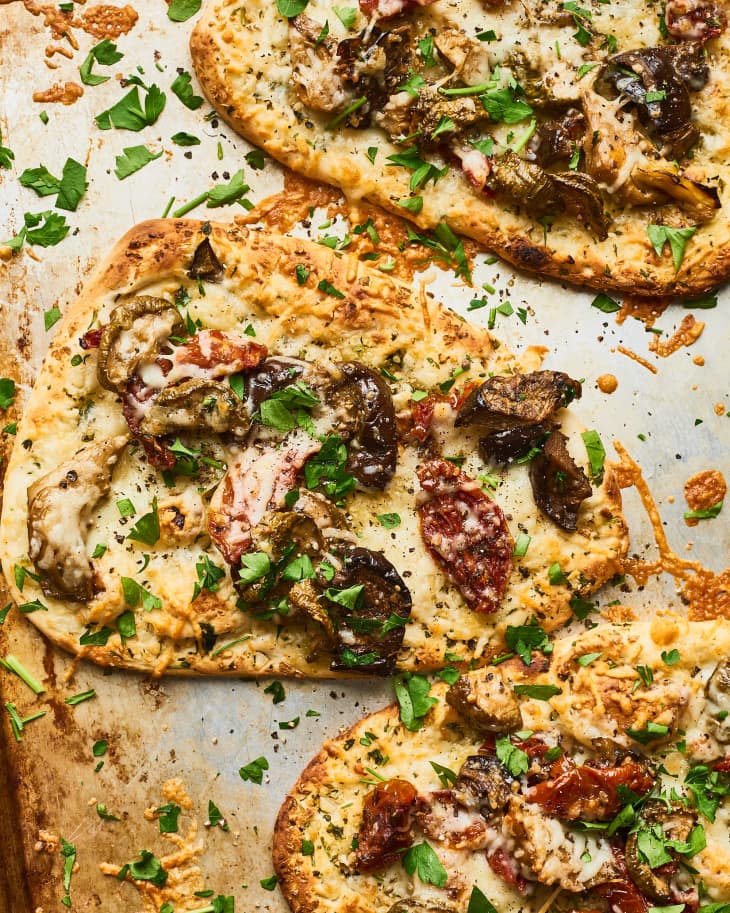 Flatbreads topped with roasted vegetables, melted cheese, and fresh parsley on a baking sheet.
