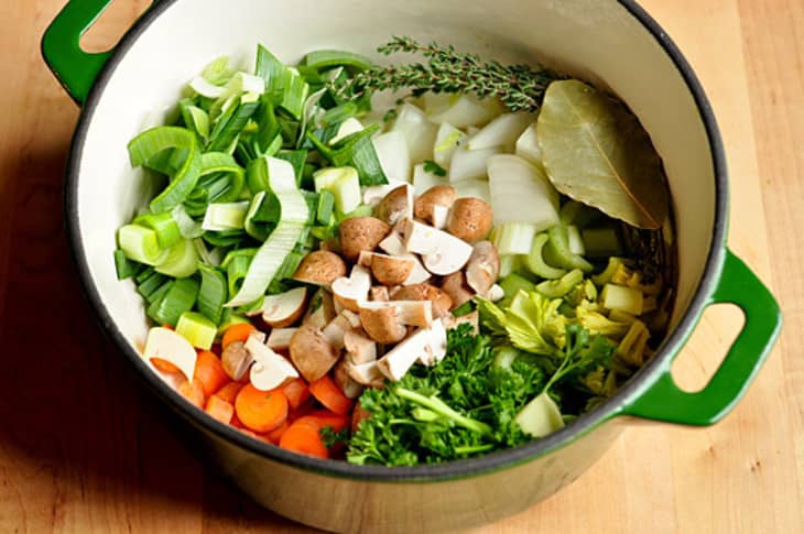 Leek, carrots, celery, onions and mushrooms chopped for vegetable broth with fresh parsley, thyme, and bay leaf all in a pot