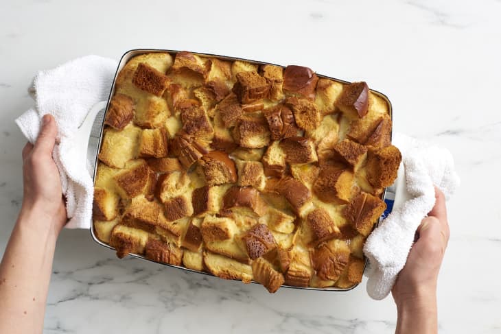 Someone holds a rectangular pan filled with sweet bread pudding on both sides