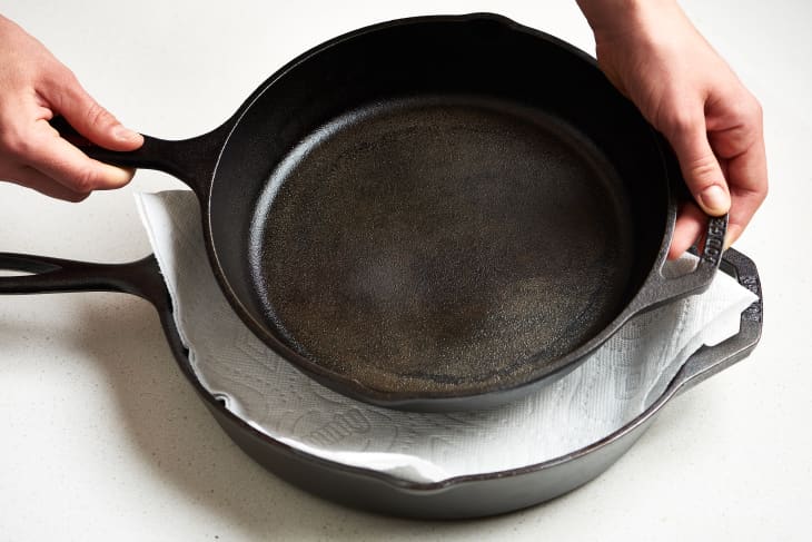 A person stacks a cast iron skillet with another  with a paper towel lining in it