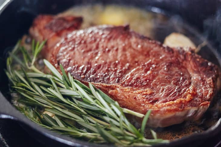 Steak in a cast-iron pan with a few sprigs of fresh rosemary