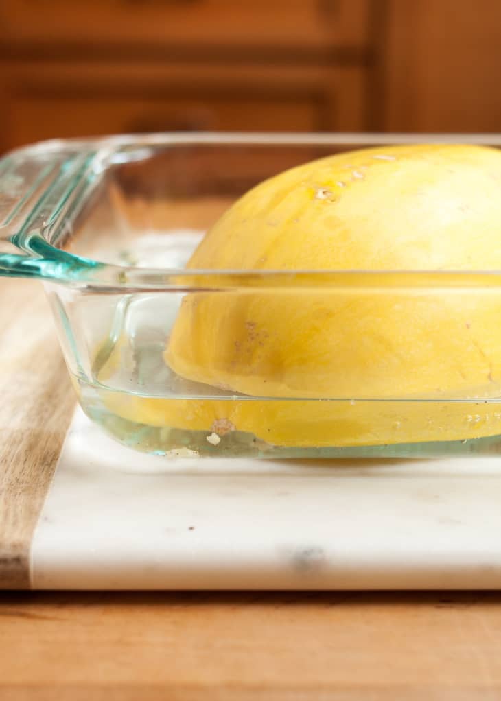 Spaghetti squash is soaked in water flesh down in a glass baking dish