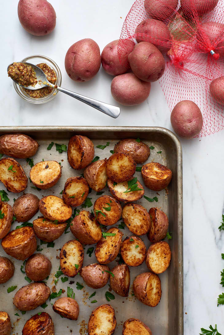 Roasted Dijon potatoes, garnished with chopped parsley, on sheet pan. In the corner there are small red potatoes and whole-grain Dijon mustard