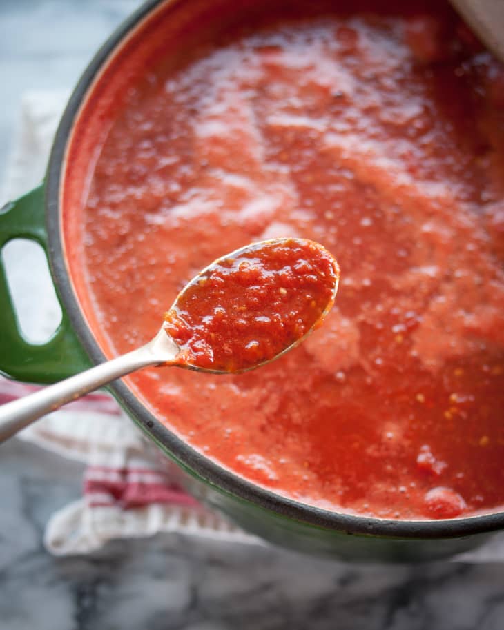 Tomato sauce cooking on the stove with a spoon filled with the sauce to show detail