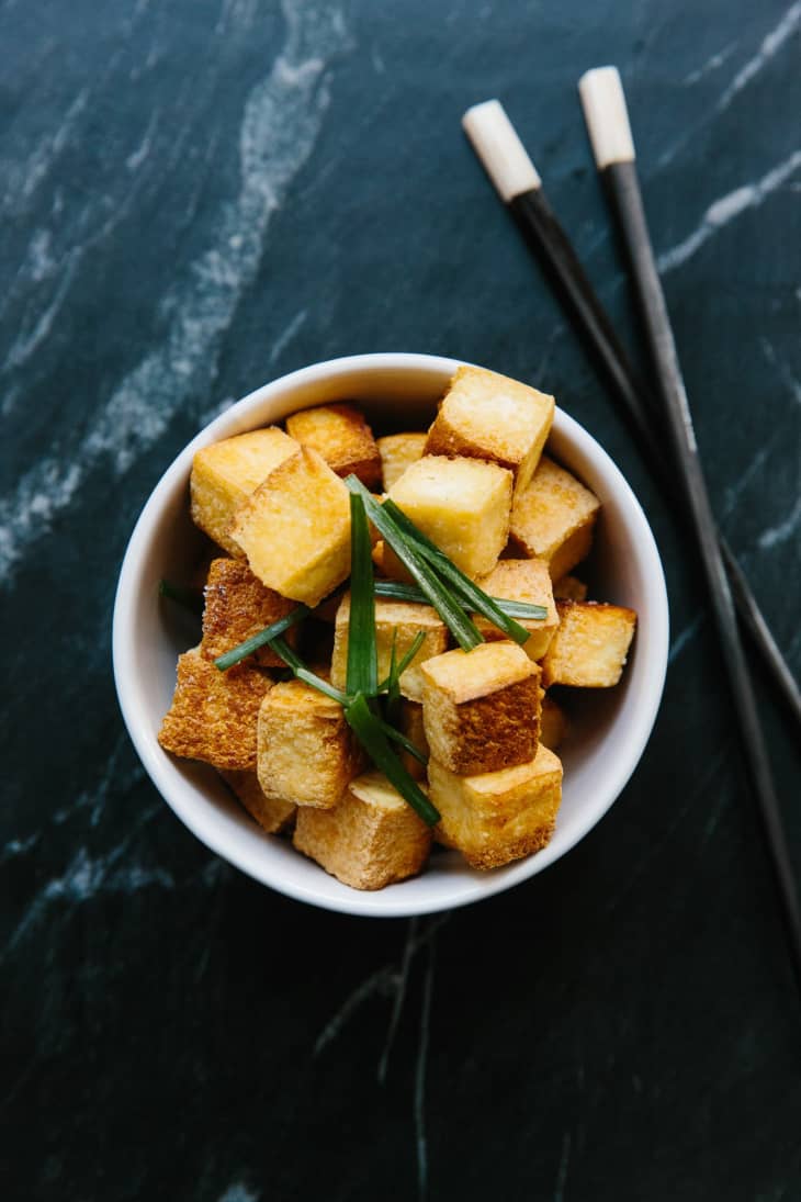 Cubes of stir-fried tofu in a bowl, with chopsticks on the side
