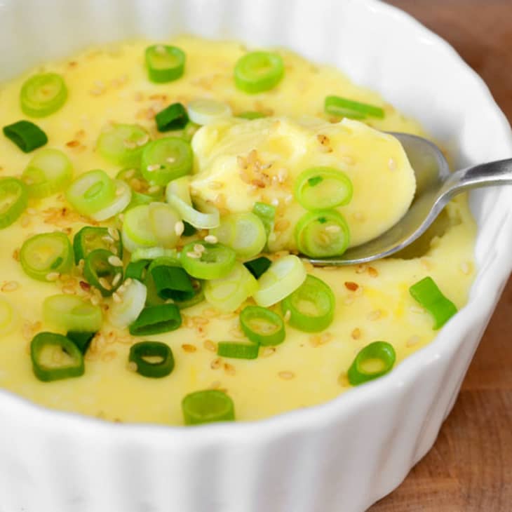 Steamed egg, garnished with scallions, in a ramekin with a spoon