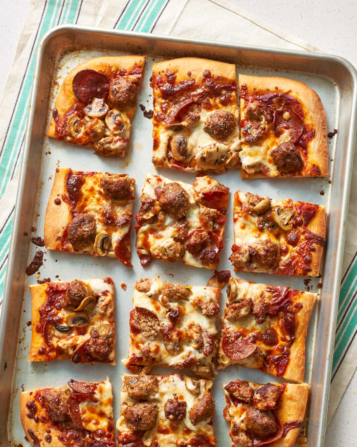 Sheet pan pizza with tomato sauce, mozzarella cheese, pepperoni, pork sausage, quartered meatballs, and mushrooms