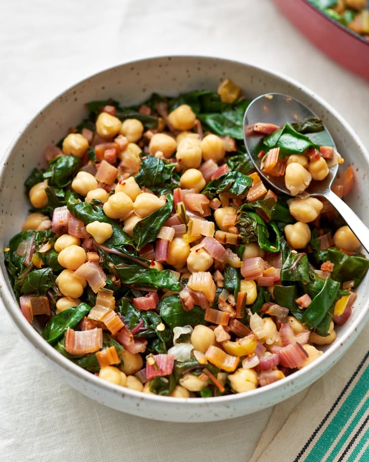 A mix of chickpeas, Swiss chard, and pancetta in a bowl with a spoon