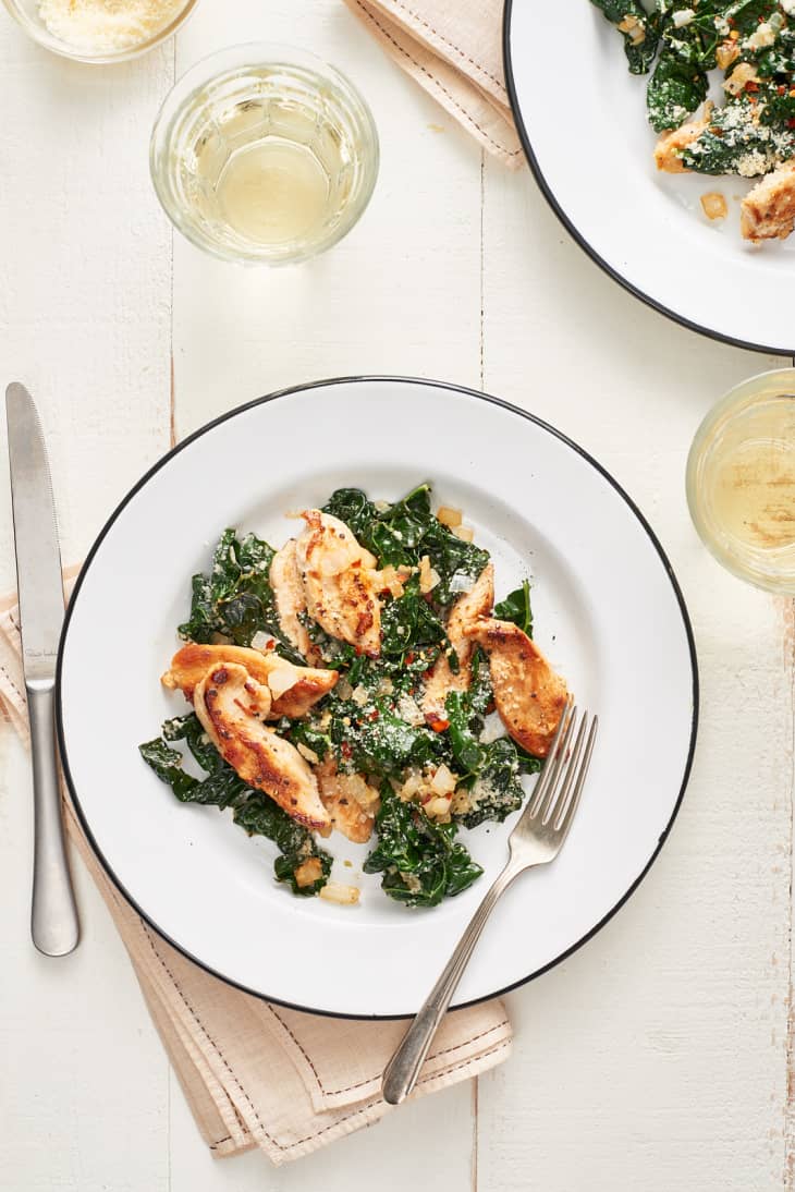 Chicken and kale sauté with Parmesan cheese on black-rimmed plate with fork and knife