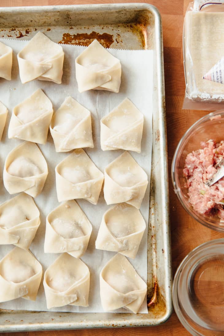 Wonton dumplings are neatly folded and lined up in a sheet pan
