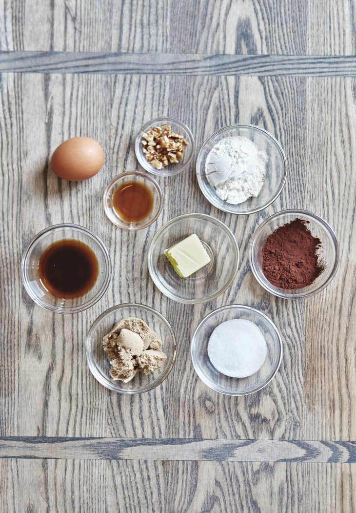 Ingredients for the brownie are placed in small bowls: unsalted butter, flour, brown sugar, granulated sugar, unsweetened cocoa powder, egg, cold coffee, vanilla extract, and chopped walnuts